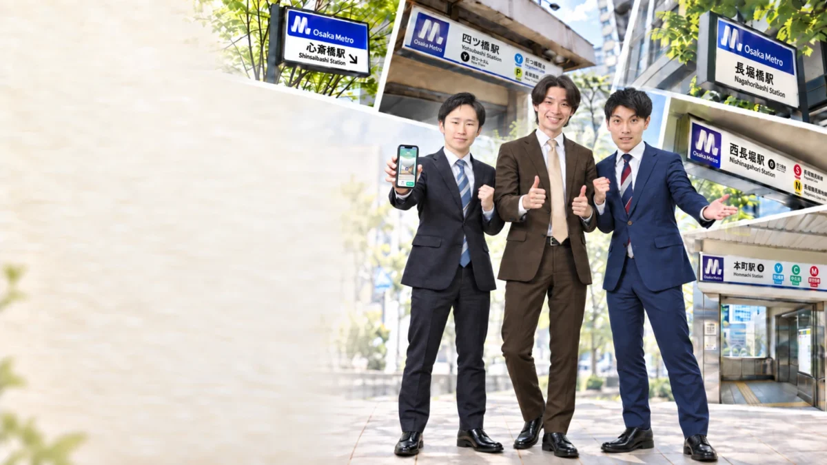 NICEROOM大阪心斎橋店のスタッフ3人。左からスタッフの栂尾、店長の岸田、スタッフの奥田。心斎橋駅や長堀橋駅など近くの駅の看板を背景に、栂尾がLINEの画面を表示したスマホを持ち、岸田が親指を立てている
